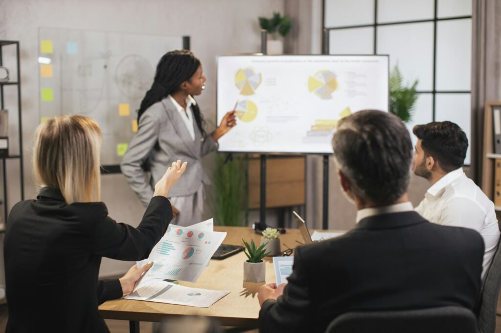 Confident African businesswoman showing statistic datas on big plasma screen for her colleagues